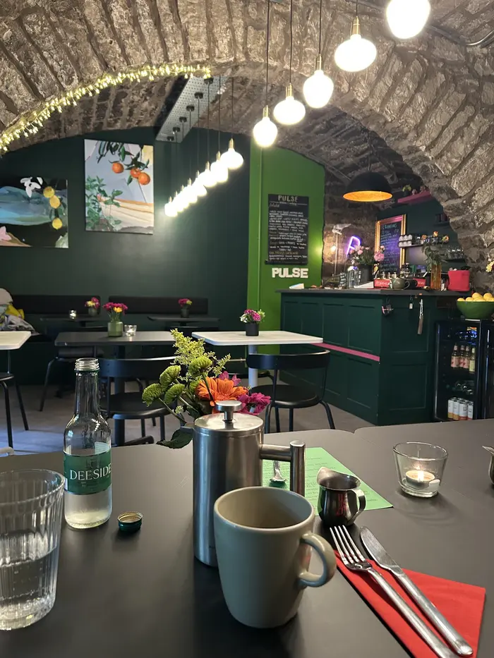 Stone-vaulted dining room with dark green walls, fairy lights and fresh flowers on every table
